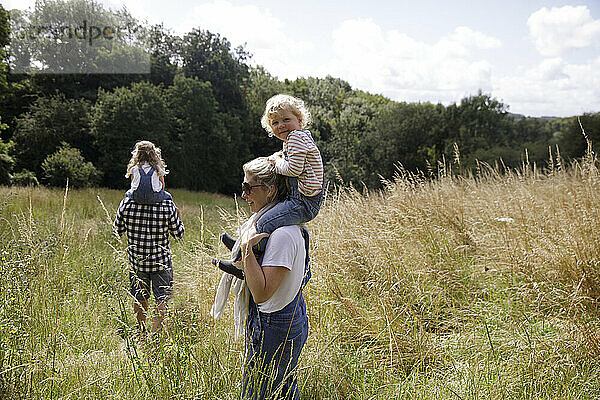 Porträt glücklich niedlichen Mädchen auf den Schultern der Mutter in sonnigen ländlichen Feld
