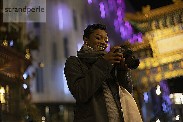Lächelnde junge Frau mit Kamera auf Stadt Straße in der Nacht