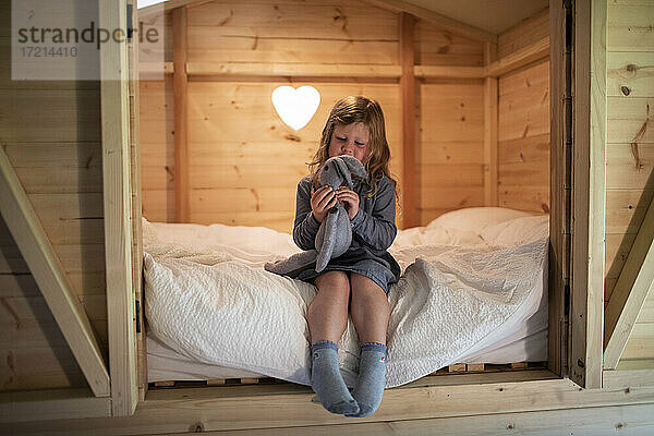 Nettes Mädchen spielt mit ausgestopften Hasen auf dem Bett in Holz Loft