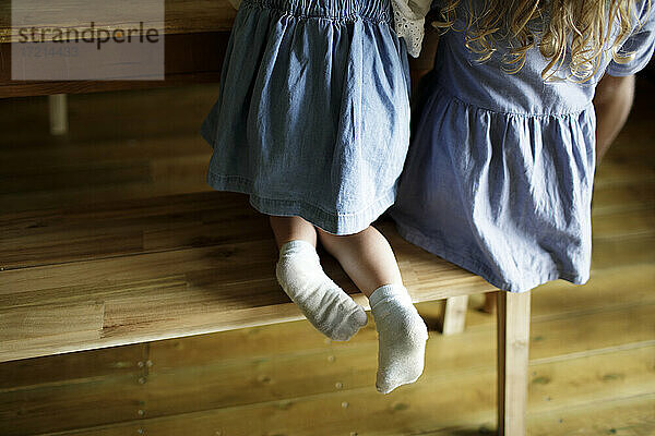 Mädchen in Jeanskleid mit schmutzigen Socken an Holz Esstisch