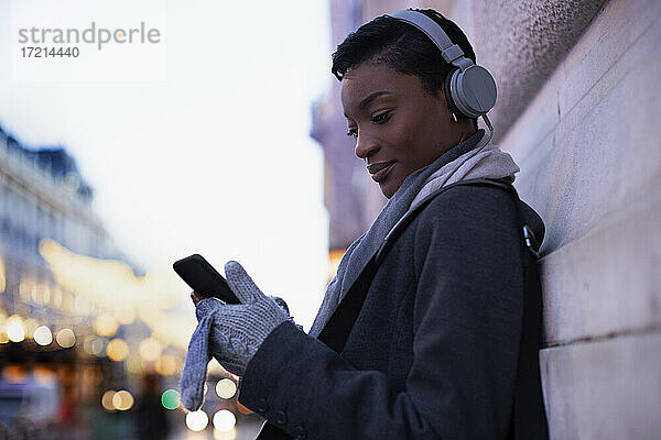 Junge Frau mit Kopfhörer mit Smartphone auf dem Bürgersteig der Stadt