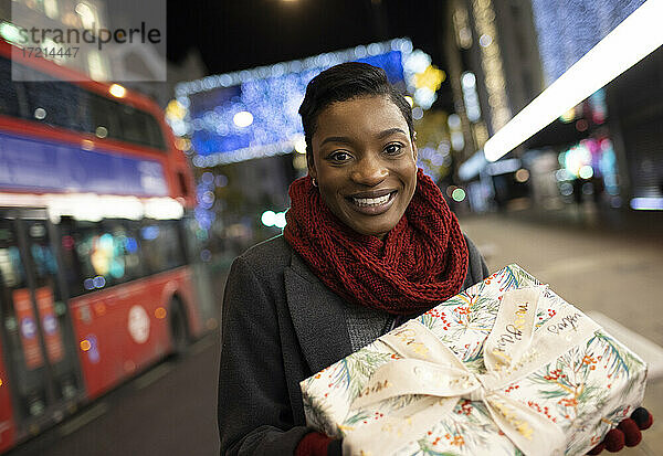 Porträt junge Frau mit Weihnachtsgeschenk auf Stadt Bürgersteig in der Nacht