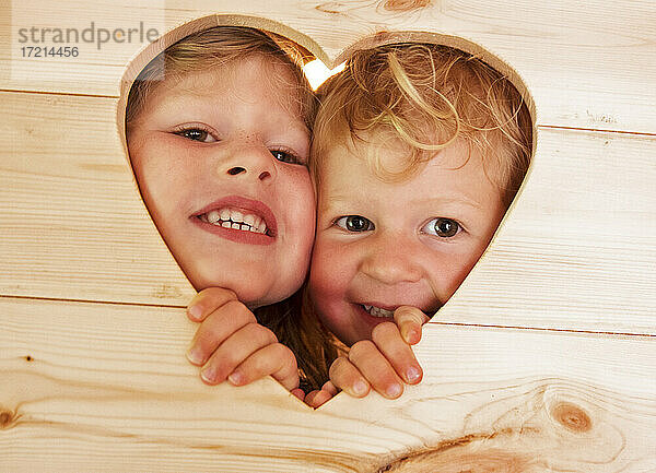 Close up Porträt niedlichen Schwestern späht durch Herzform in Holz
