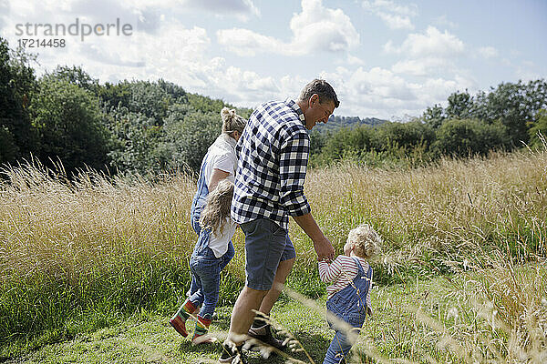 Familie hält Hände zu Fuß in sonnigen ländlichen Sommer Feld