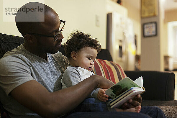 Vater liest dem Baby auf dem Sofa vor