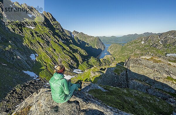 Wanderin  junge Frau sitzt auf Felsen  Boot im Fjord Trollfjord  Berge und Raftsund  Lofoten  Nordland  Norwegen  Europa