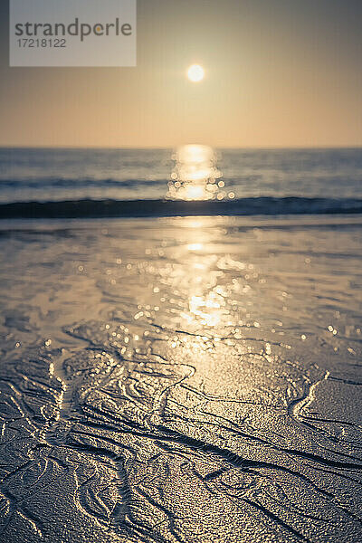 Tief stehende Abendsonne über der Nordsee vor der Insel Sylt. Im Vordergrund bildet das ablaufende Wasser Muster aus kleinen Rinnsalen im Sand
