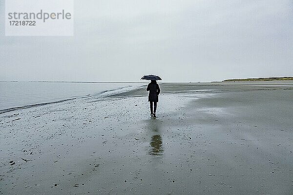 Frau mit Schirm spaziert am Strand bei Regenwetter  Langeoog  Ostfriesische Inseln  Niedersachsen  Deutschland  Europa