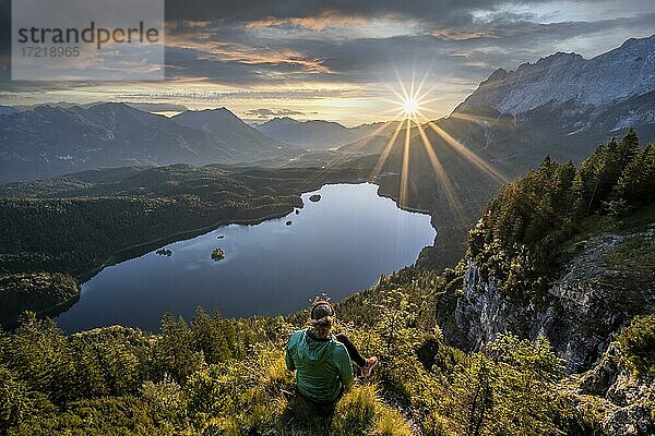 Wanderin blickt auf Eibsee bei Sonnenaufgang  Sonne scheint über Bayrisches Voralpenland  rechts Zugspitze  Wettersteingebirge bei Grainau  Oberbayern  Bayern  Deutschland  Europa