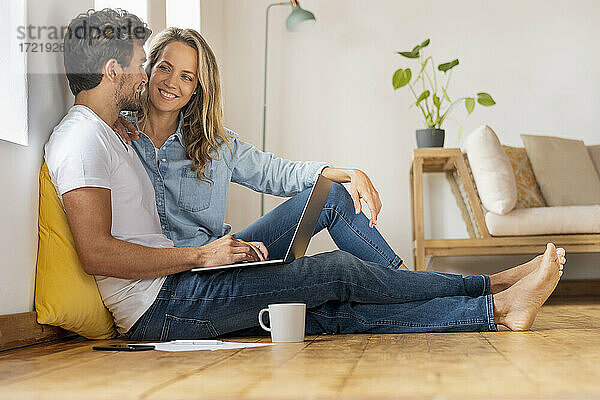 Glückliches Paar mit Laptop  das sich gegenseitig ansieht  während es zu Hause im Büro sitzt