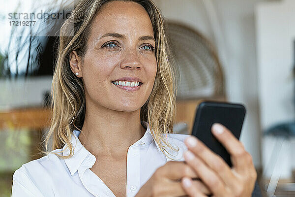 Lächelnde schöne Frau hält Handy zu Hause