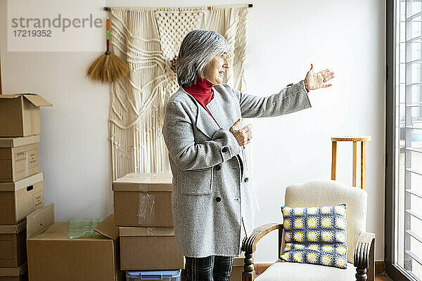 Ältere Frau mit weißen Haaren gestikuliert vor ihrem neuen Haus