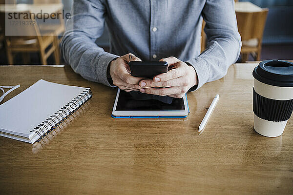 Geschäftsmann  der ein Smartphone über ein digitales Tablet auf einem Schreibtisch am Arbeitsplatz benutzt