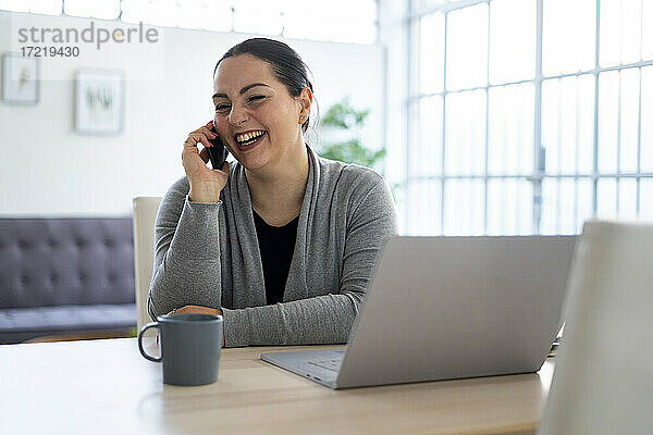 Geschäftsfrau lacht  während sie zu Hause mit dem Handy telefoniert