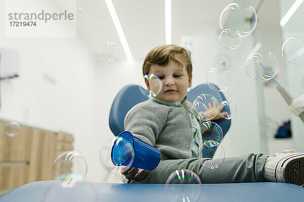 Junge spielt mit Glas  während er in der Klinik mit Seifenblasen herum sitzt