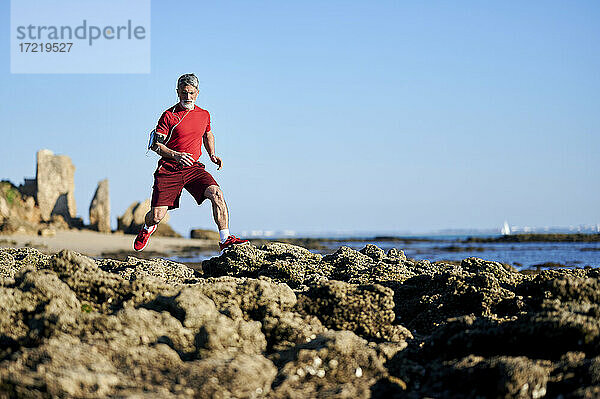 Älterer Mann läuft auf Felsen am Strand