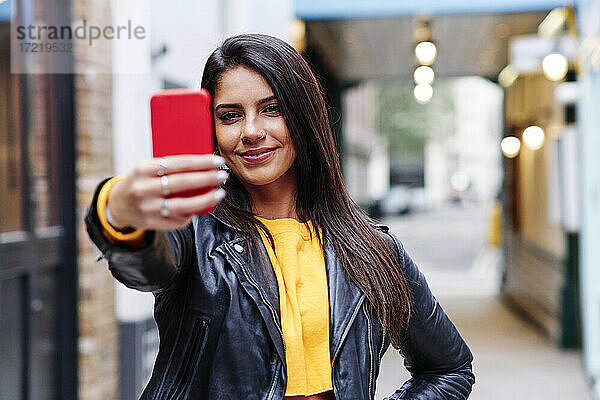 Lächelnde Frau nimmt Selfie durch Handy in der Stadt