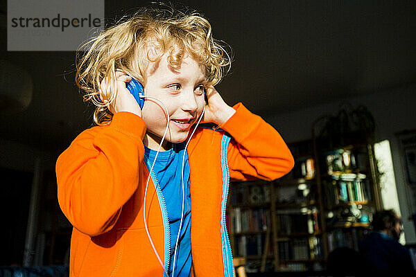 Blonder Junge schaut weg  während er zu Hause über Kopfhörer Musik hört