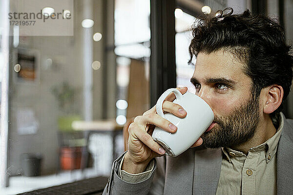 Männlicher Freiberufler trinkt Kaffee in einem beleuchteten Cafe