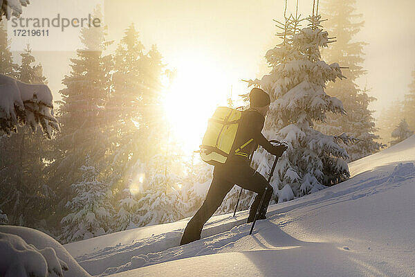 Mann Skitour auf verschneitem Berg bei Sonnenaufgang