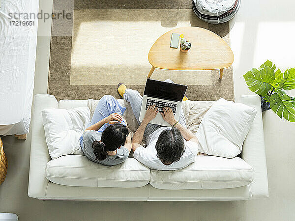 Paar benutzt einen Laptop  während es zu Hause auf dem Sofa sitzt