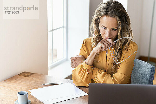 Weibliche Fachkraft hält eine Brille und schaut auf einen Laptop auf dem Schreibtisch