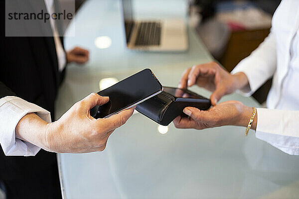 Rezeptionistin mit Kreditkartenlesegerät  während ein Kunde an der Hotelrezeption kontaktlos bezahlt