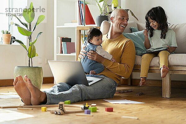Lächelnder Vater mit Laptop  der mit seinen Töchtern zu Hause spielt