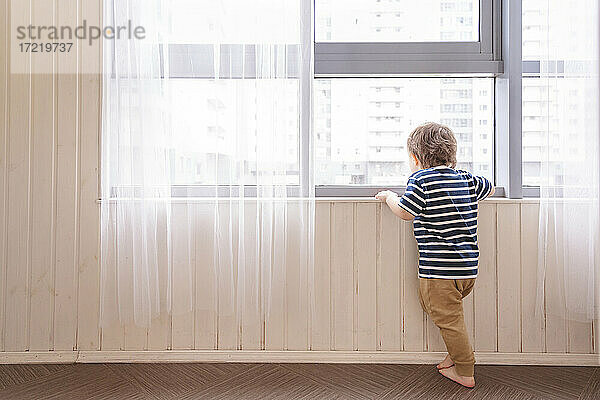 Junge schaut durch das Fenster  während er zu Hause steht