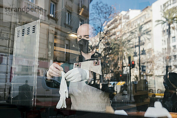 Mann mit Schutzhandschuhen durch Glas in Restaurant gesehen