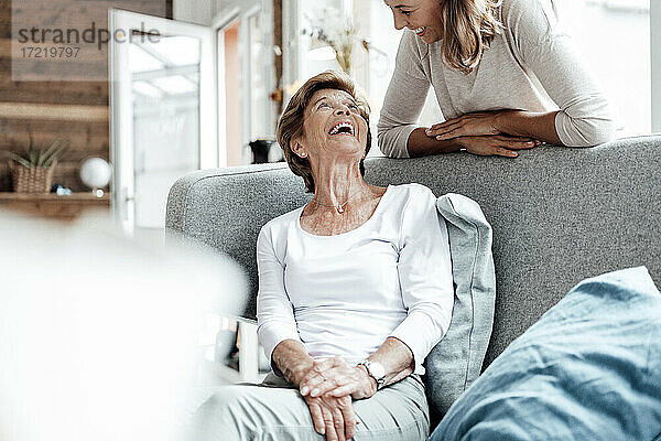 Lachende Großmutter  die ihre Enkelin an das Sofa lehnt