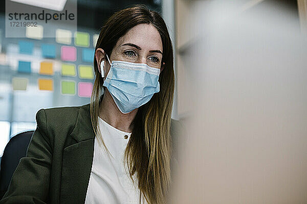 Unternehmerin mit Gesichtsschutzmaske bei der Arbeit im Büro während COVID-19