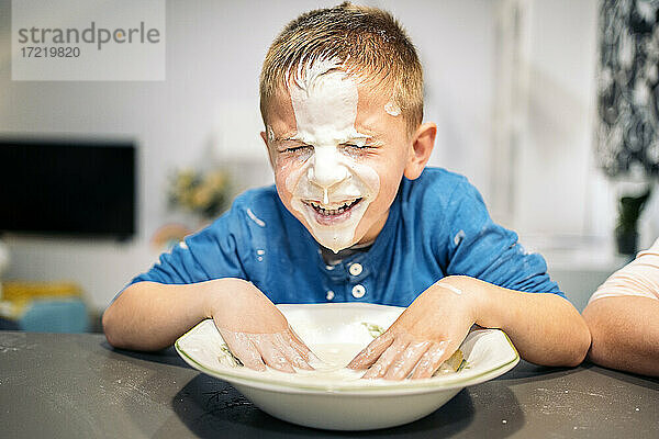 Lächelnder Junge  der sich zu Hause das Gesicht mit Mehl und Wasser einschmiert
