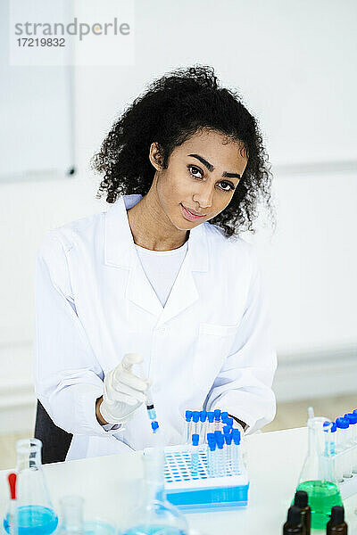 Junge Forscherin hält Spritze an Reagenzglas bei der Arbeit im Labor