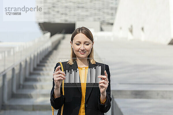 Lächelnde Geschäftsfrau im mittleren Erwachsenenalter  die ein futuristisches digitales Tablet im Freien benutzt