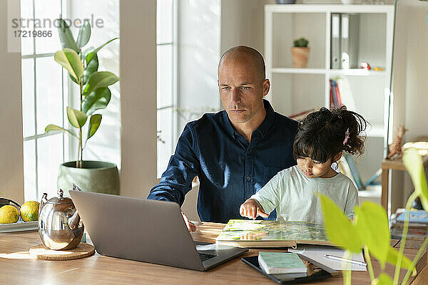 Männlicher Unternehmer  der mit seiner Tochter an einem Laptop arbeitet  während er zu Hause arbeitet