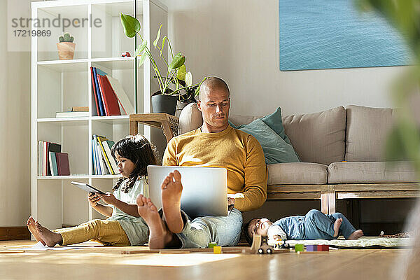 Vater arbeitet am Laptop  während er bei seinen Töchtern zu Hause sitzt