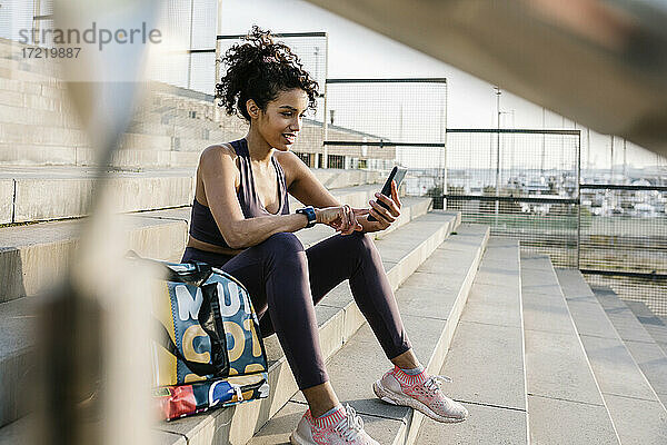 Eine Sportlerin benutzt ein Mobiltelefon  während sie auf einer Treppe sitzt