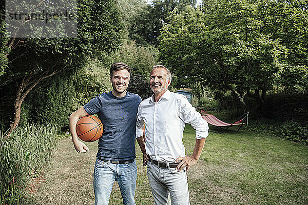 Lächelnder Sohn mit Basketball stehend mit Vater im Hinterhof
