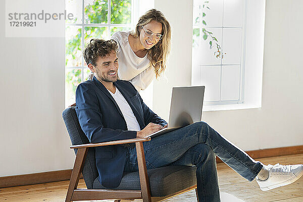 Mann benutzt Laptop  während er bei seiner Freundin zu Hause auf dem Stuhl sitzt