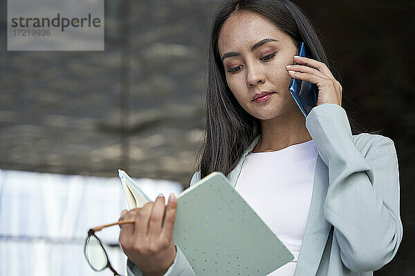 Geschäftsfrau liest Tagebuch  während sie mit dem Handy telefoniert