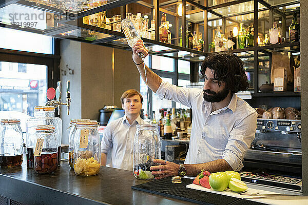 Männlicher Barkeeper gießt Alkohol in ein Fruchtglas am Bartresen