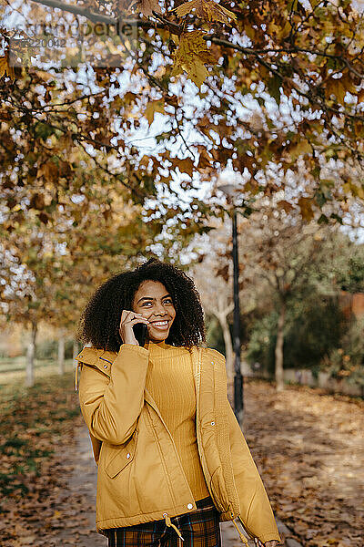Glückliche Afro-Frau  die im Herbst in einem öffentlichen Park mit einem Smartphone telefoniert