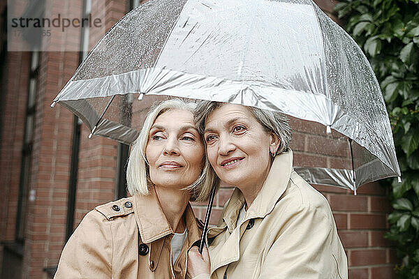 Lächelnde Freundinnen unter Regenschirm an einem regnerischen Tag