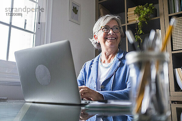 Glückliche Geschäftsfrau  die wegschaut  während sie zu Hause mit ihrem Laptop arbeitet