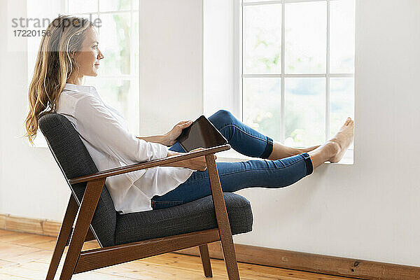 Blonde Frau  die auf einem Sessel zu Hause sitzt und nachdenkt
