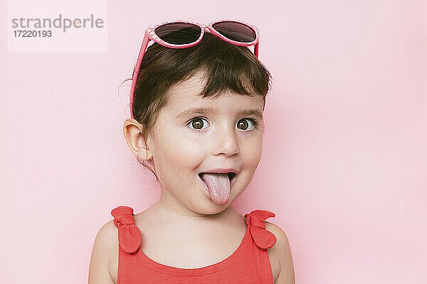 Porträt eines kleinen Mädchens  das seine Zunge vor einem rosa Hintergrund herausstreckt