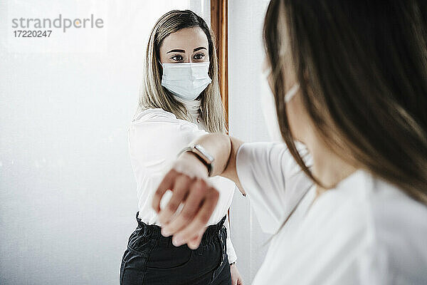 Weibliche Patientin mit Gesichtsschutzmaske beim Ellbogenstoß mit dem Arzt im Krankenhaus