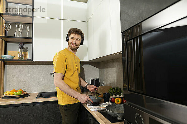 Lächelnder Mann hört Musik bei der Zubereitung von Essen in der Küche zu Hause