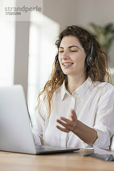 Zufriedene weibliche Kundendienstmitarbeiterin mit Kopfhörern  die einem Kunden am Schreibtisch im Heimbüro etwas erklärt